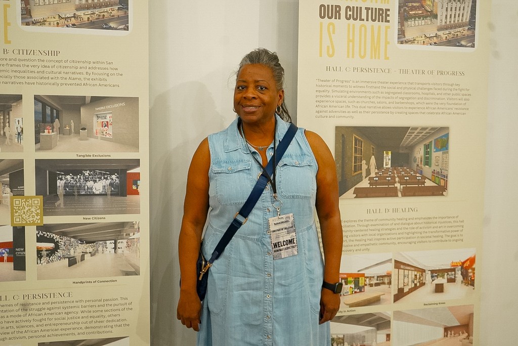 A woman in a denim dress stands in front of informative exhibit panels at an event related to cultural heritage and citizenship.